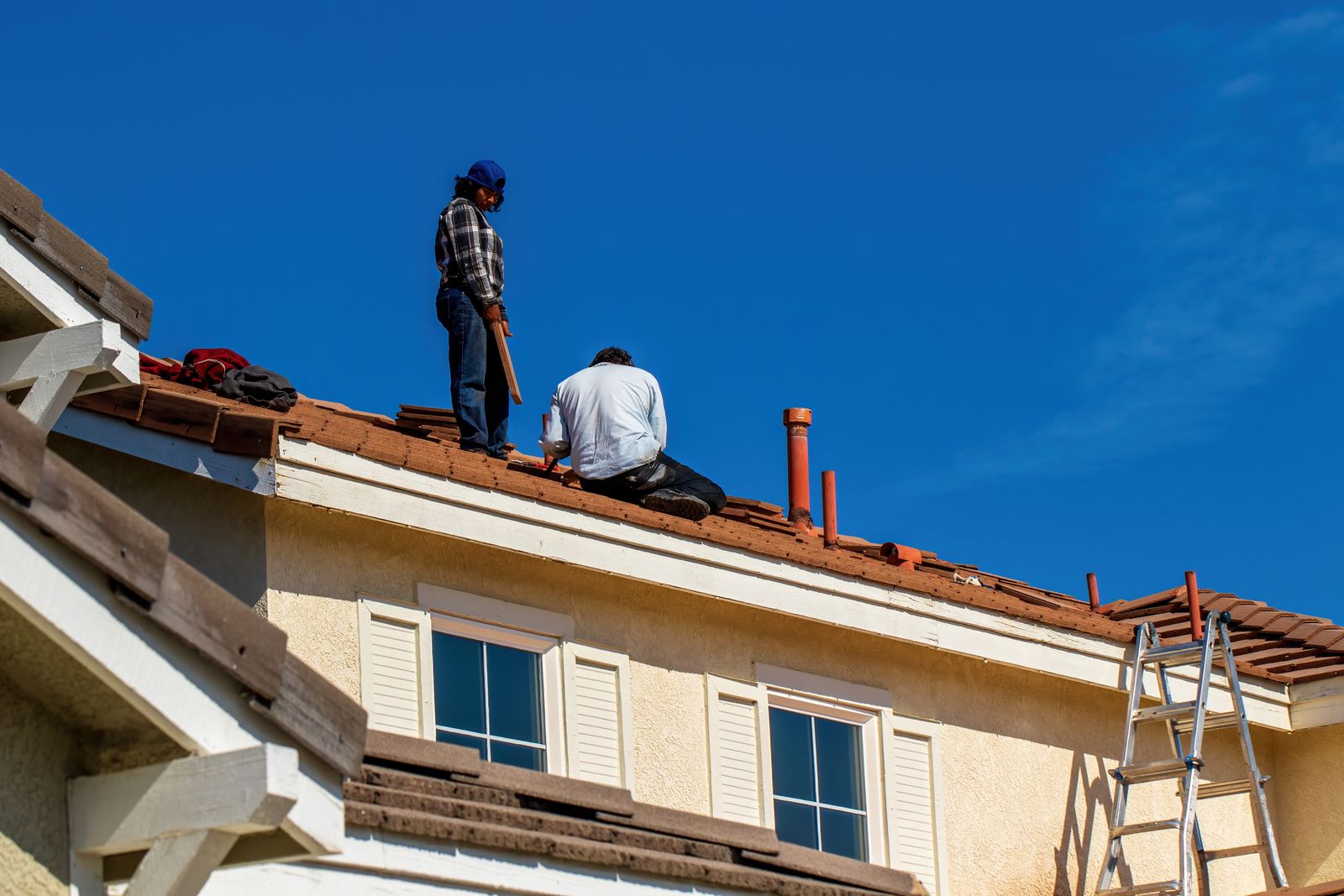 Roofers at work on a tile roof under a clear sky