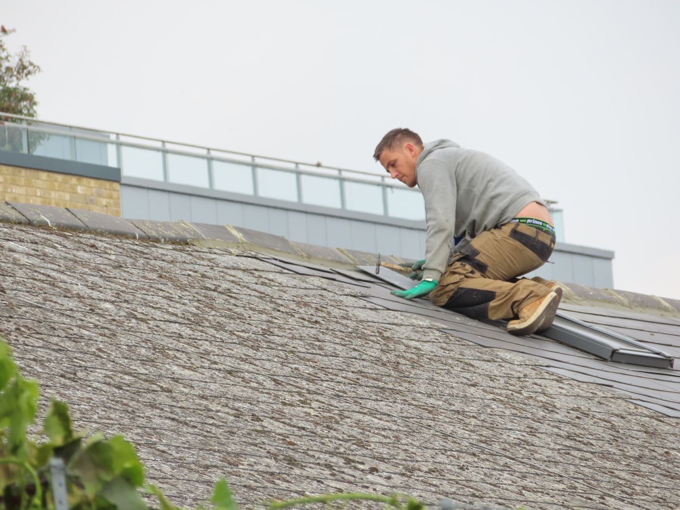 A roofer kneeling on a shingle roof, fitting new shingles
